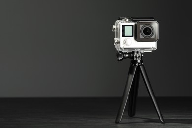 Modern action camera and tripod on grey wooden table. Space for text