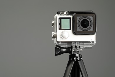 Modern action camera and tripod on grey background, closeup. Space for text