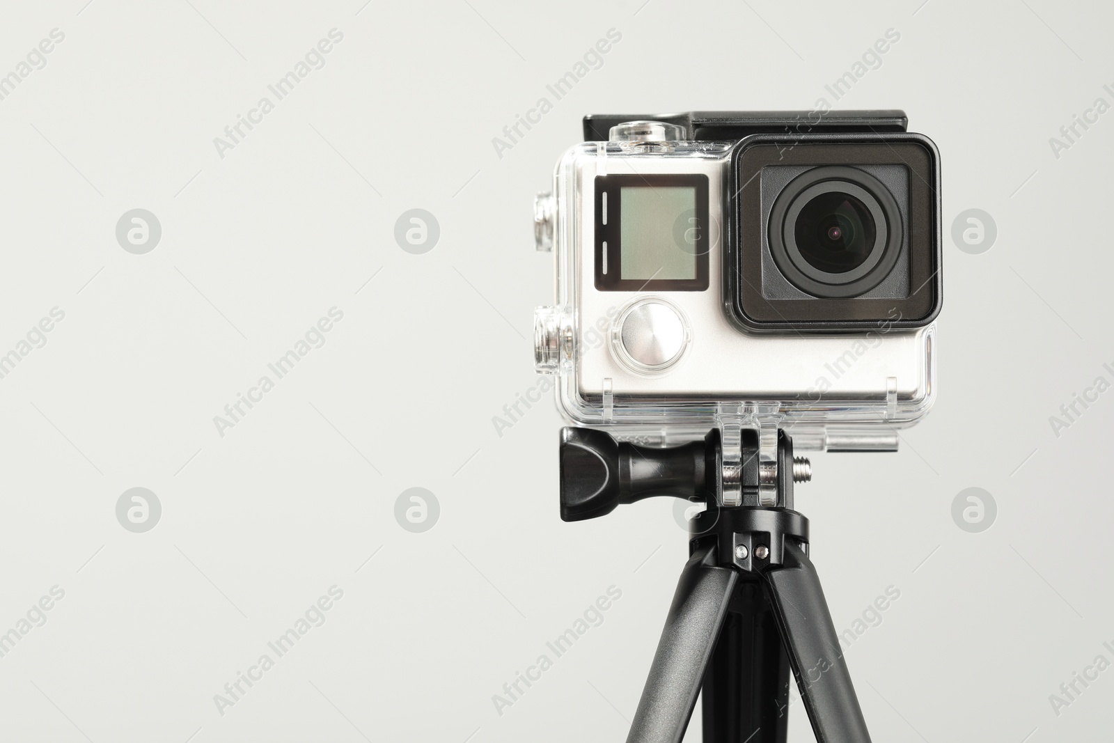 Photo of Modern action camera and tripod on light background. Space for text