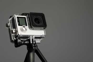 Photo of Modern action camera and tripod on grey background, closeup. Space for text