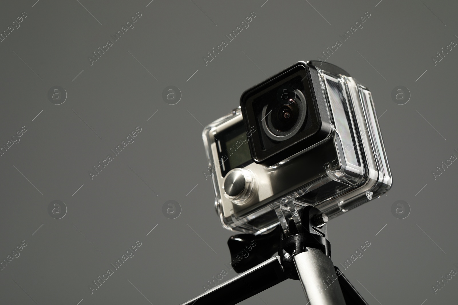 Photo of Modern action camera and tripod on grey background, closeup. Space for text