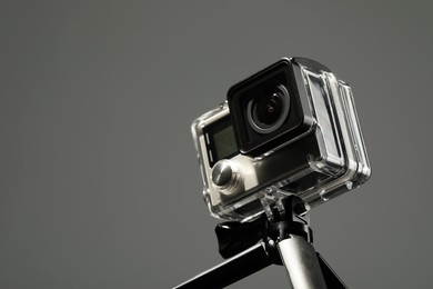 Photo of Modern action camera and tripod on grey background, closeup. Space for text