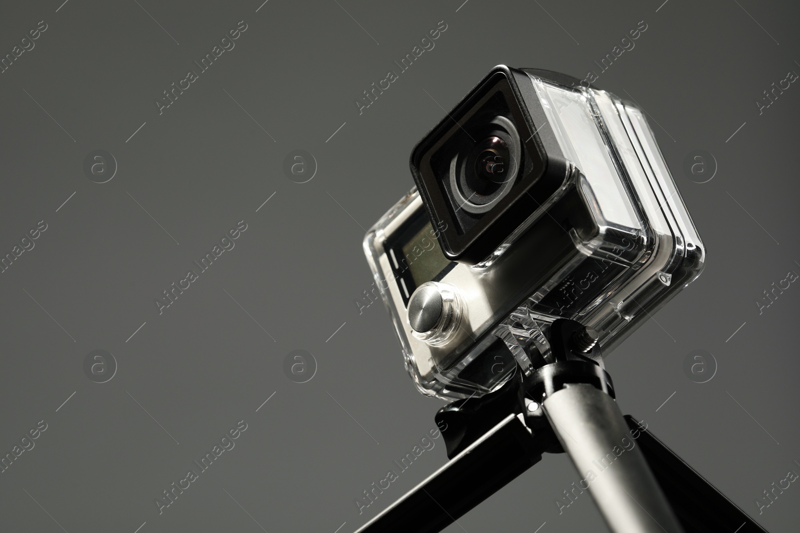 Photo of Modern action camera and tripod on grey background, closeup. Space for text