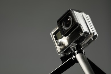 Modern action camera and tripod on grey background, closeup. Space for text