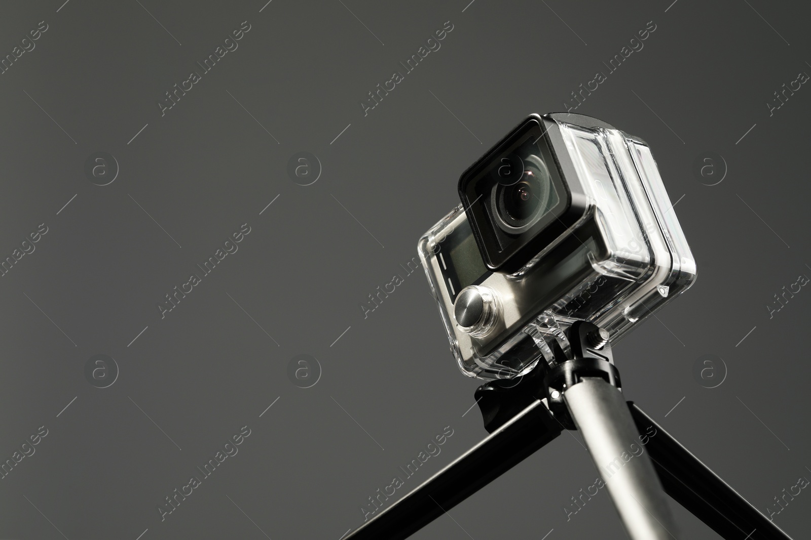 Photo of Modern action camera and tripod on grey background, closeup. Space for text