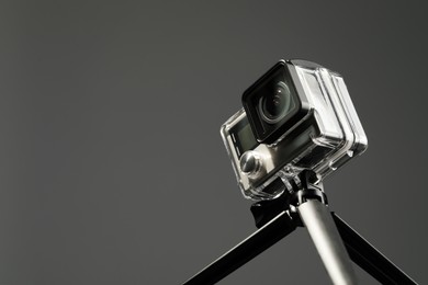 Photo of Modern action camera and tripod on grey background, closeup. Space for text