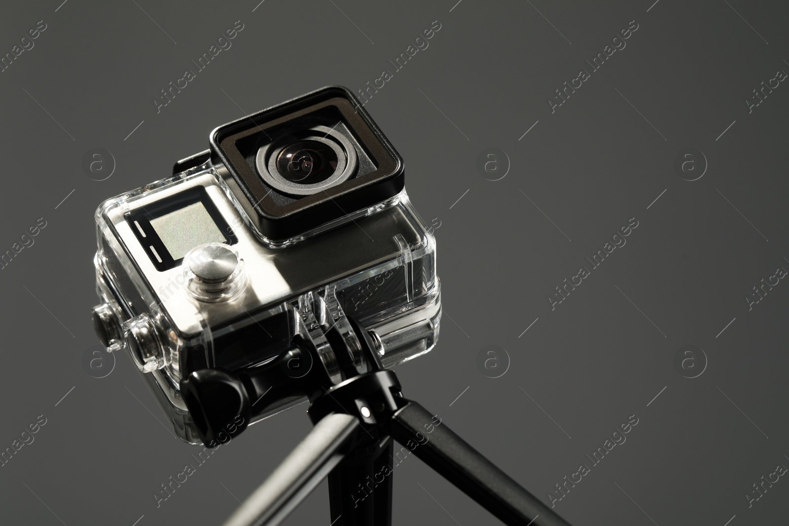 Photo of Modern action camera and tripod on grey background, closeup. Space for text