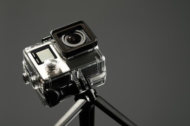 Modern action camera and tripod on grey background, closeup. Space for text