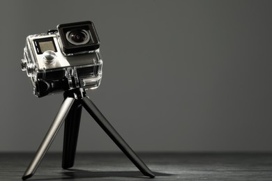 Photo of Modern action camera and tripod on grey wooden table. Space for text