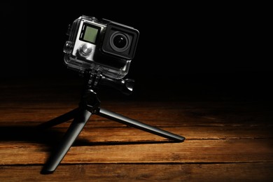 Photo of Modern action camera and tripod on wooden surface against black background. Space for text