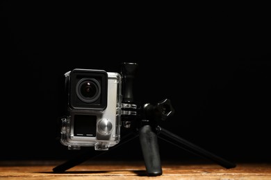 Photo of Modern action camera and tripod on wooden surface against black background