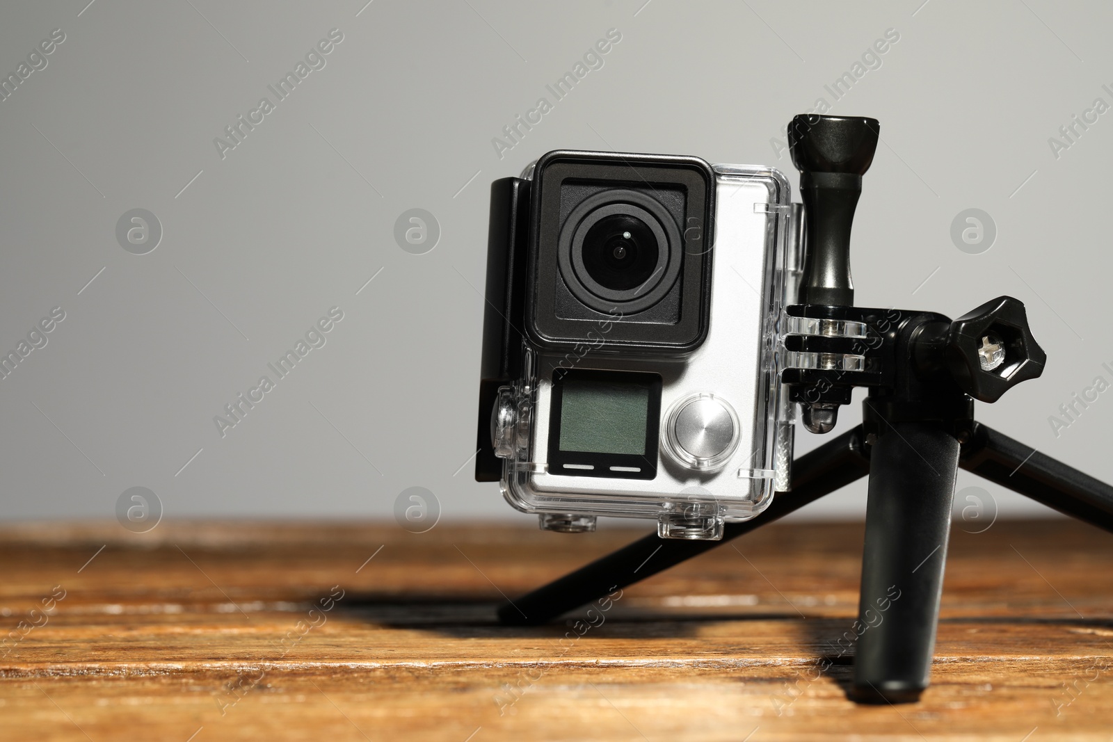 Photo of Modern action camera and tripod on wooden surface against grey background, closeup. Space for text