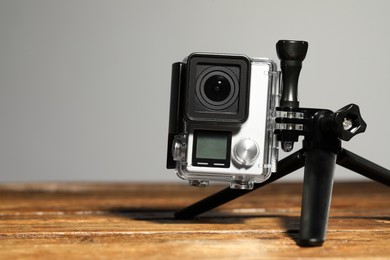 Modern action camera and tripod on wooden surface against grey background, closeup. Space for text