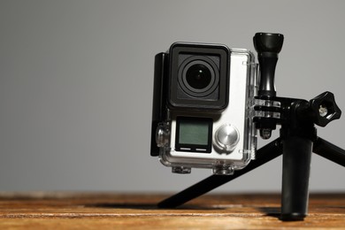 Photo of Modern action camera and tripod on wooden surface against grey background, closeup. Space for text