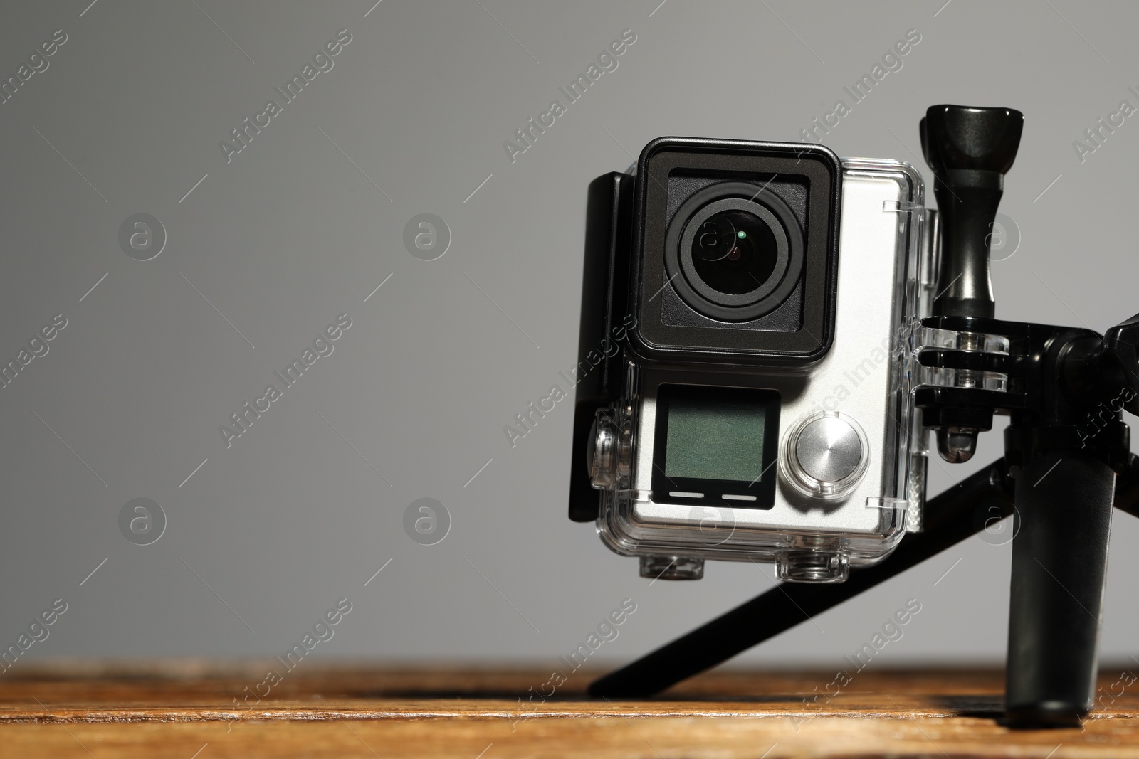 Photo of Modern action camera and tripod on wooden surface against grey background, closeup. Space for text