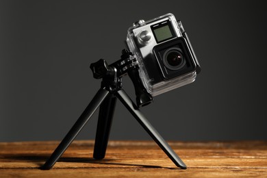 Modern action camera and tripod on wooden surface against grey background