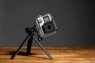 Photo of Modern action camera and tripod on wooden surface against grey background