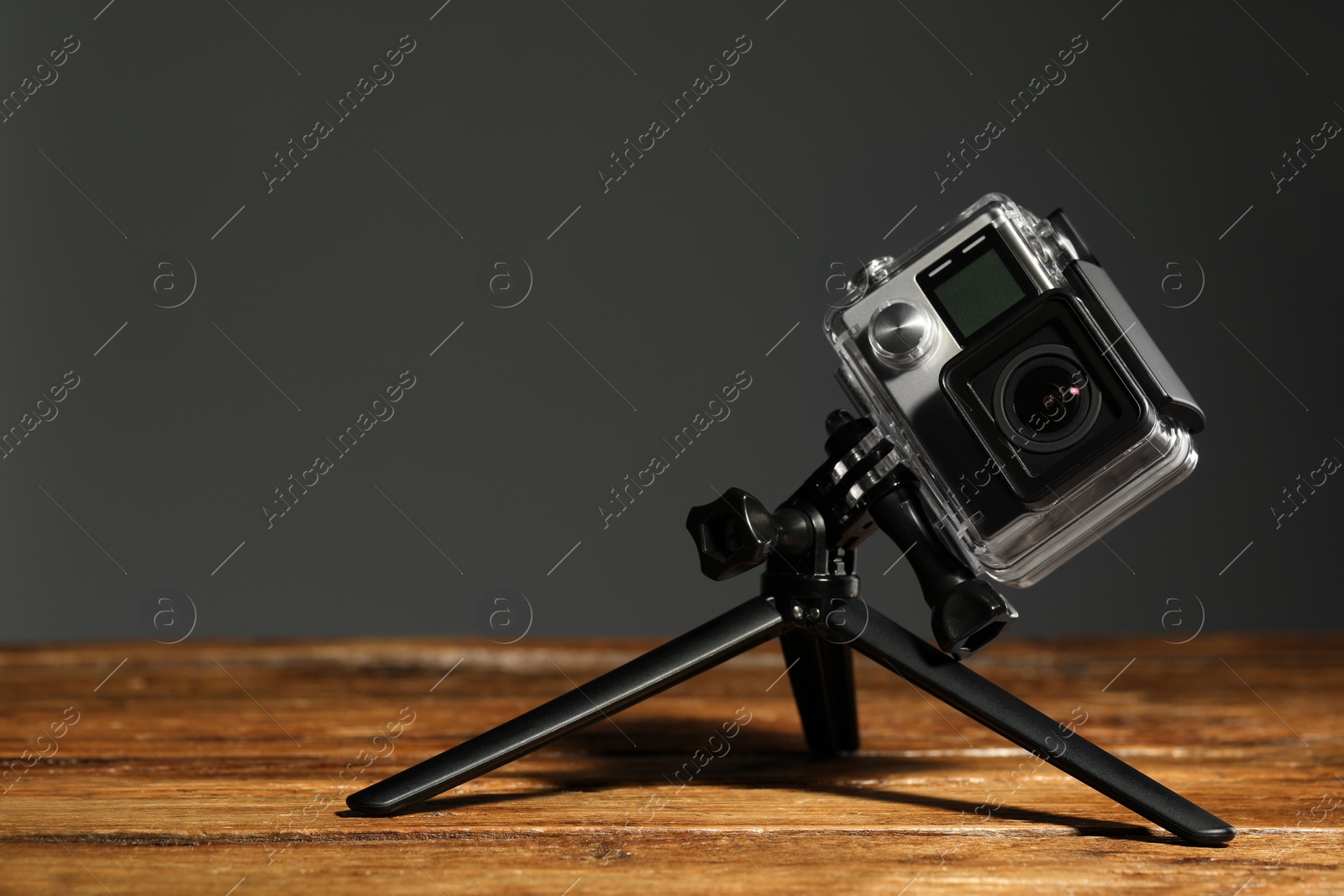 Photo of Modern action camera and tripod on wooden surface against grey background. Space for text