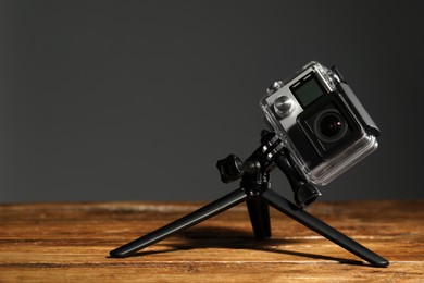 Modern action camera and tripod on wooden surface against grey background. Space for text