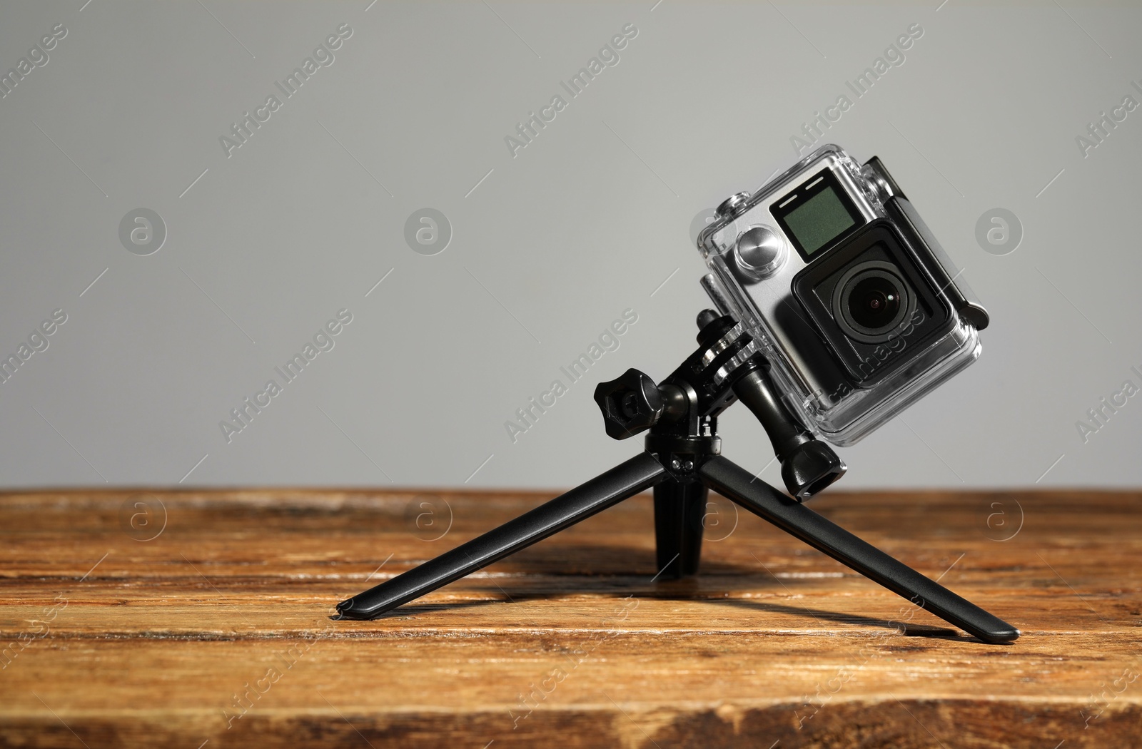 Photo of Modern action camera and tripod on wooden surface against grey background. Space for text