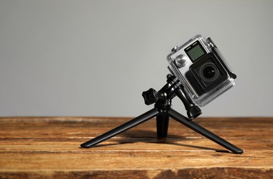 Photo of Modern action camera and tripod on wooden surface against grey background. Space for text