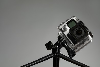 Modern action camera and tripod against grey background, closeup. Space for text