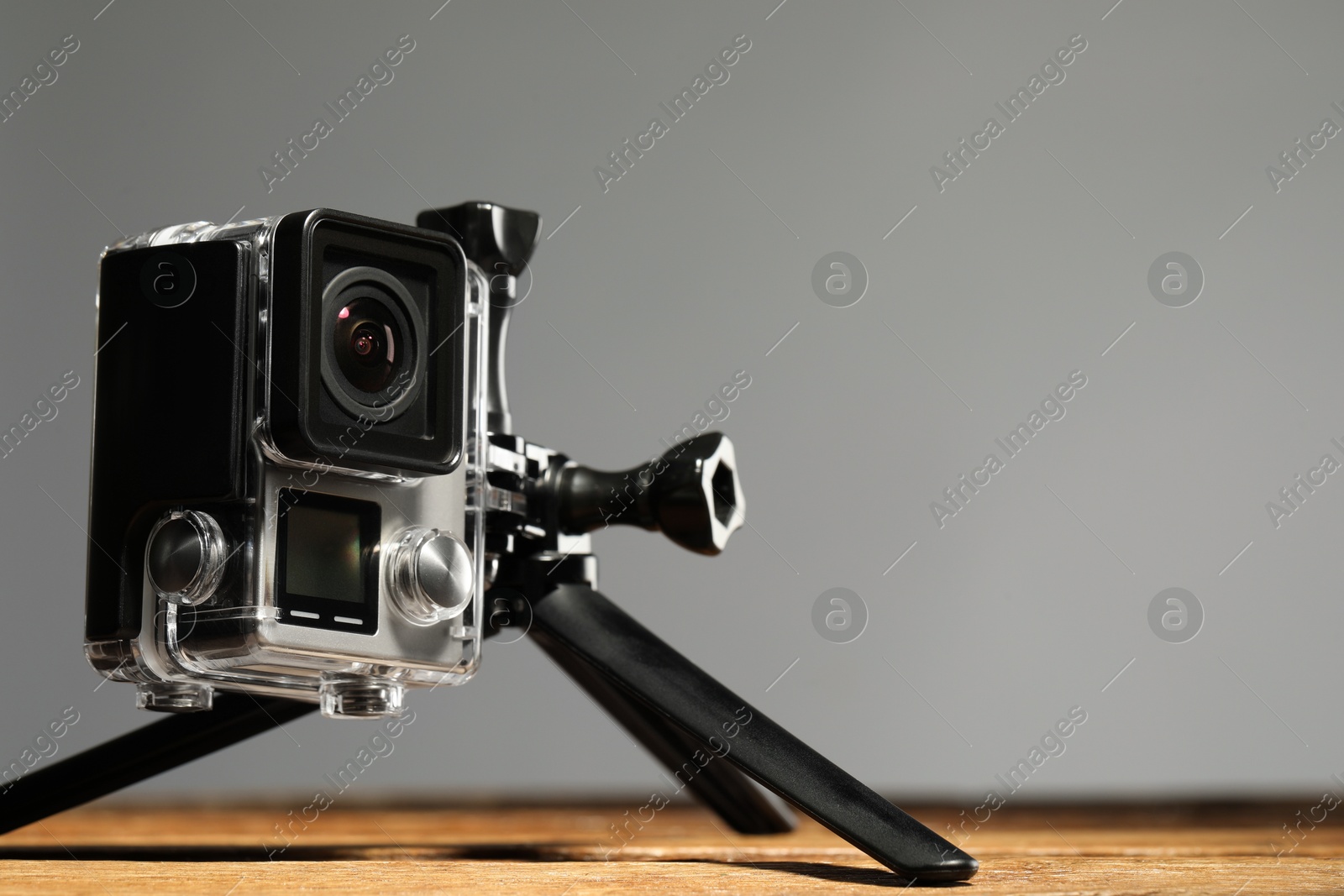 Photo of Modern action camera and tripod on wooden surface against grey background, closeup. Space for text