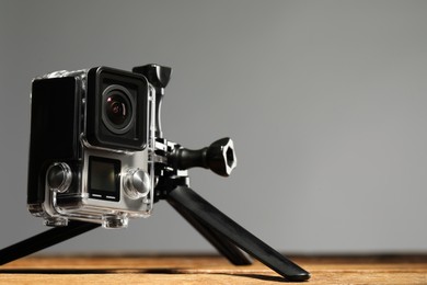 Modern action camera and tripod on wooden surface against grey background, closeup. Space for text