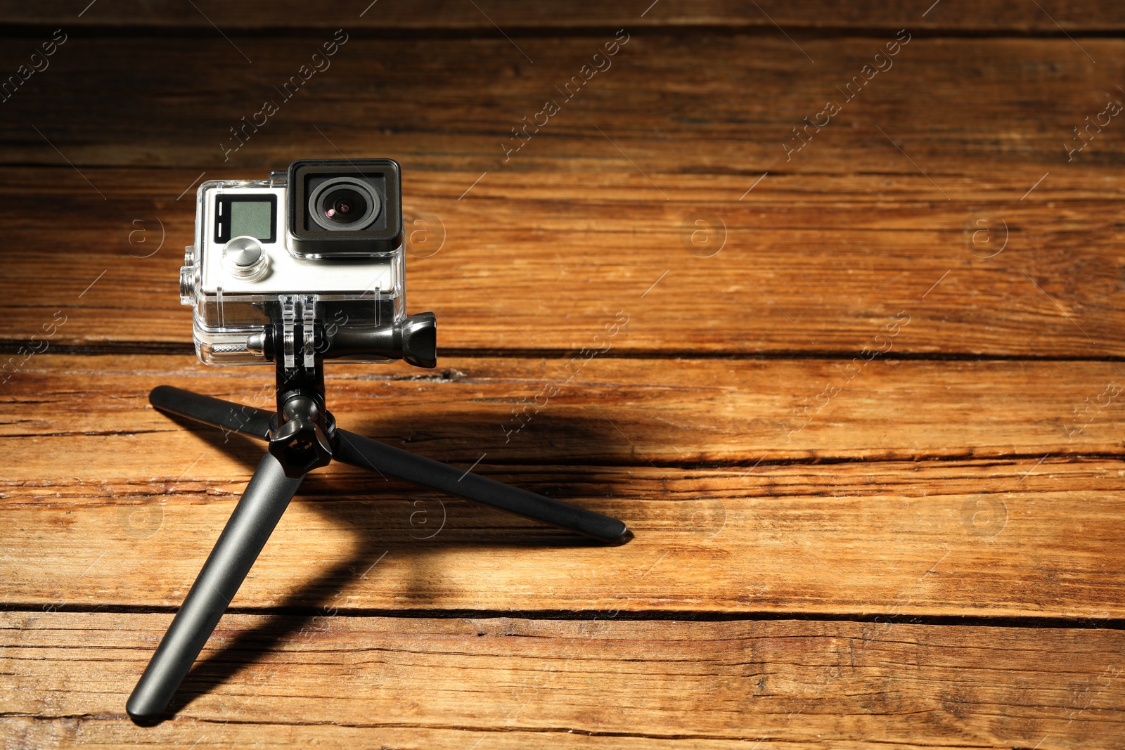 Photo of Modern action camera and tripod on wooden surface. Space for text