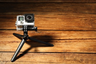 Modern action camera and tripod on wooden surface. Space for text