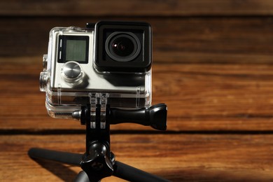 Modern action camera and tripod on wooden surface, closeup. Space for text