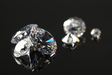 Photo of Many beautiful shiny diamonds on black mirror surface, closeup