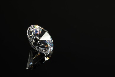 Photo of Beautiful shiny diamond on black mirror surface, closeup. Space for text