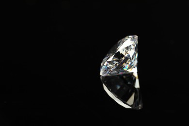 Photo of Beautiful shiny diamond on black mirror surface, closeup. Space for text