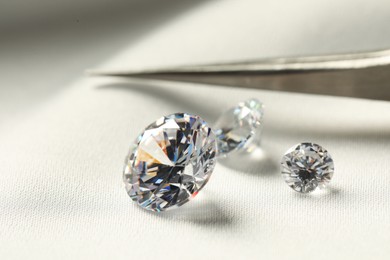 Beautiful shiny diamonds and tweezers on white fabric, closeup