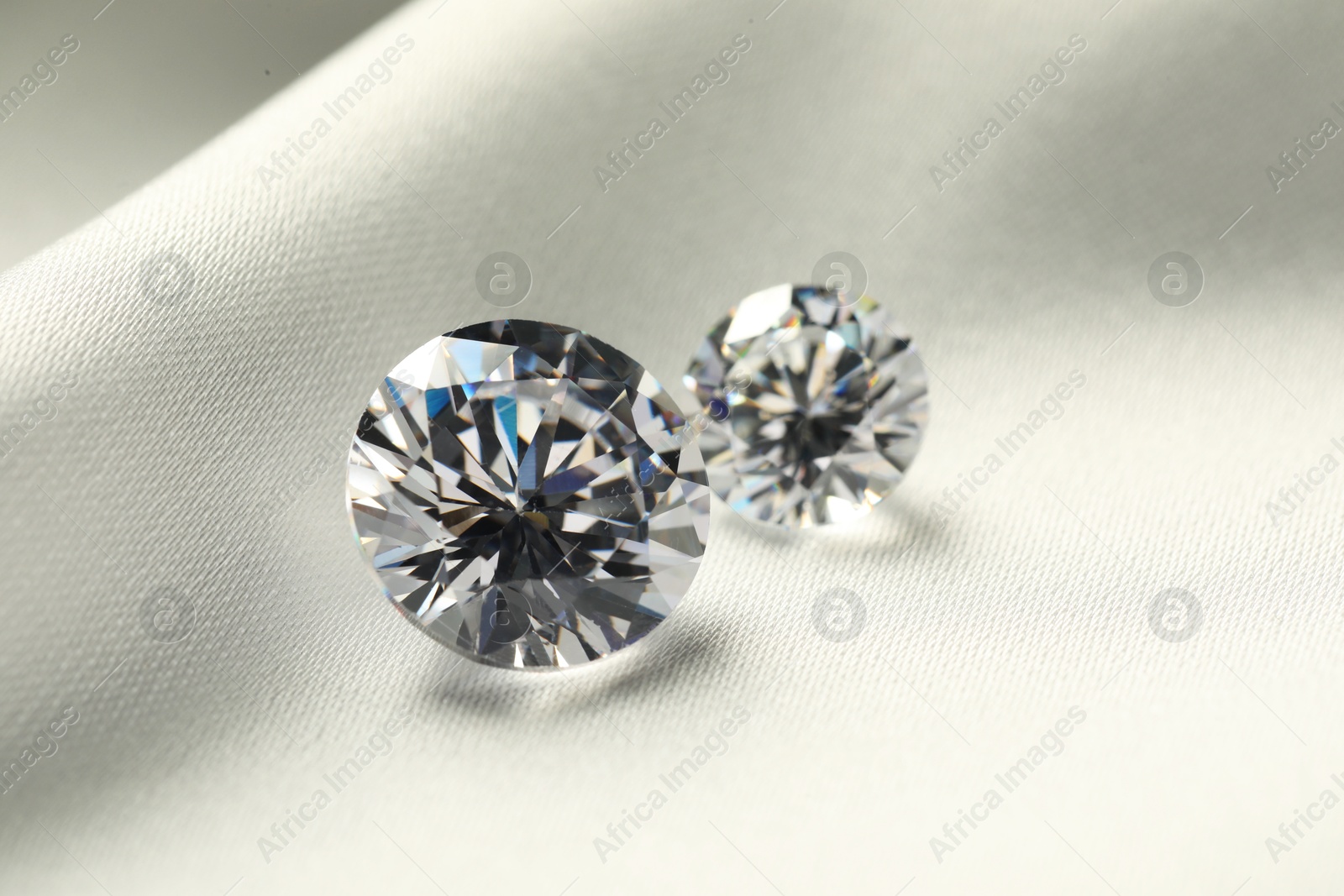 Photo of Two beautiful shiny diamonds on white fabric, closeup