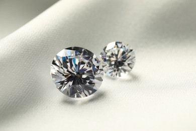 Photo of Two beautiful shiny diamonds on white fabric, closeup