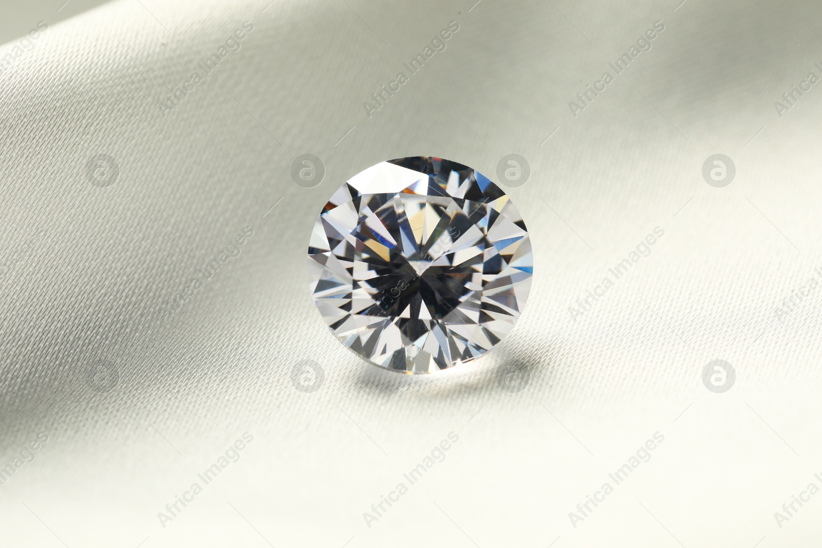 Photo of One beautiful shiny diamond on white fabric, closeup