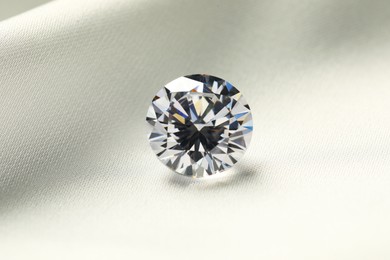 Photo of One beautiful shiny diamond on white fabric, closeup