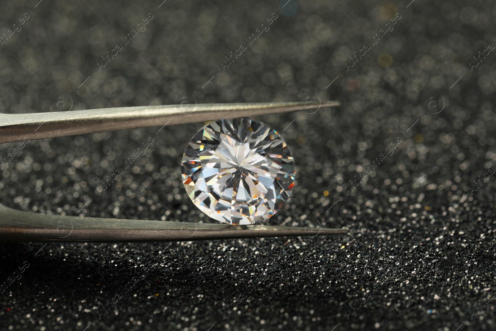 Photo of Tweezers with beautiful diamond on dark shiny background, closeup