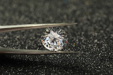 Tweezers with beautiful diamond on dark shiny background, closeup