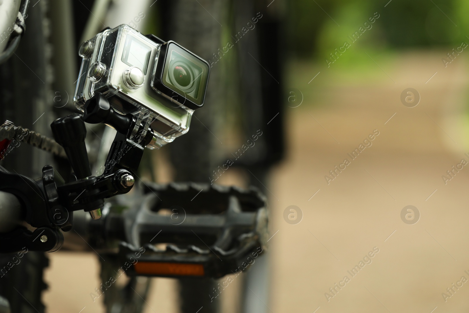 Photo of Modern action camera with mount on bicycle outdoors, closeup. Space for text