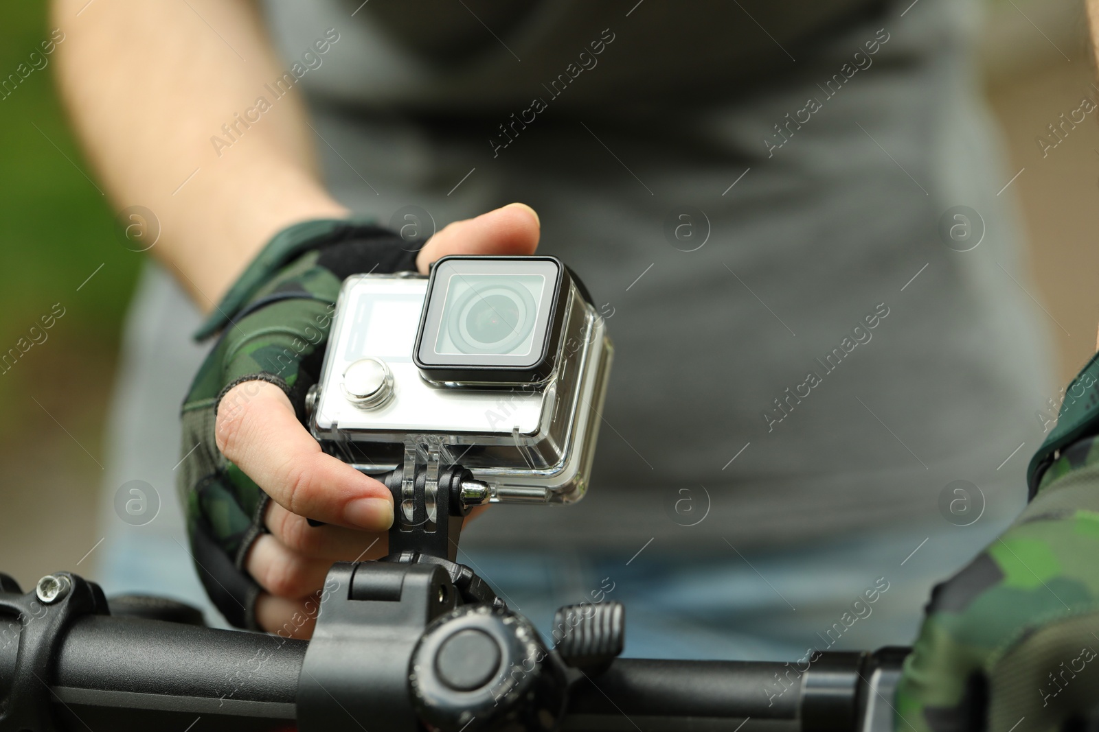 Photo of Man riding bicycle with modern action camera outdoors, closeup