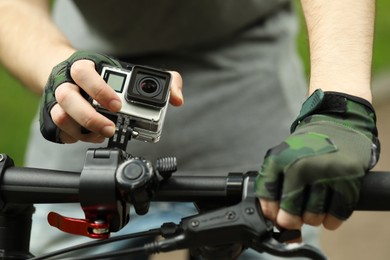 Photo of Man riding bicycle with modern action camera outdoors, closeup