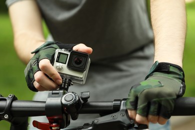 Photo of Man riding bicycle with modern action camera outdoors, closeup