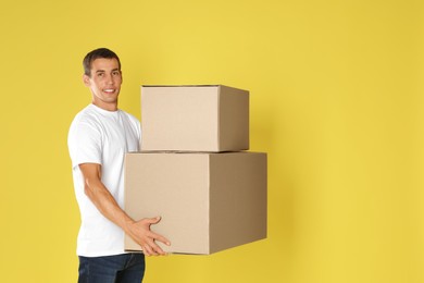 Photo of Moving into new house. Man with cardboard boxes on yellow background, space for text