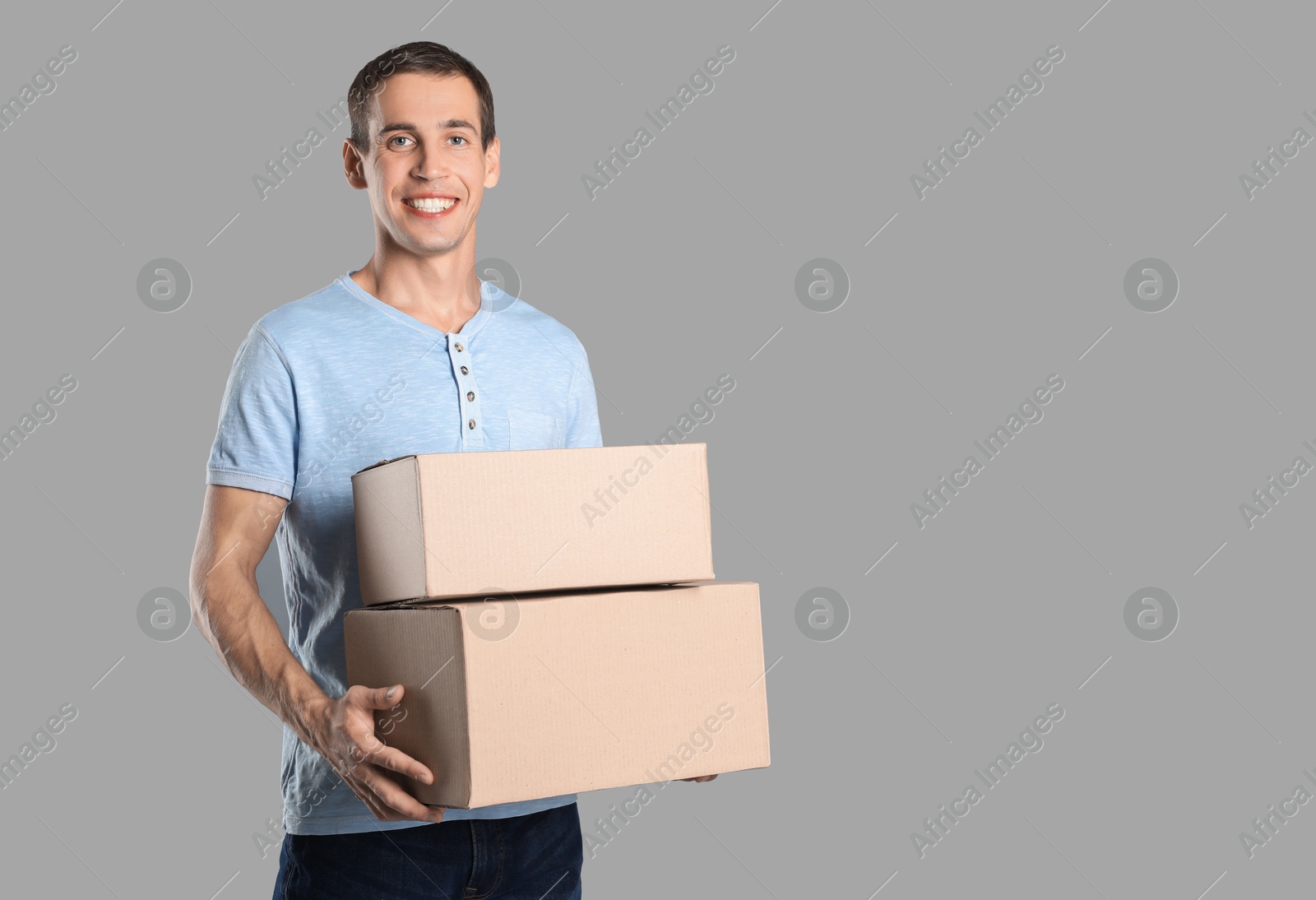 Photo of Moving into new house. Man with cardboard boxes on grey background, space for text