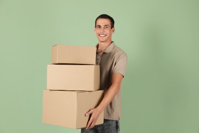 Moving into new house. Man with cardboard boxes on light green background, space for text