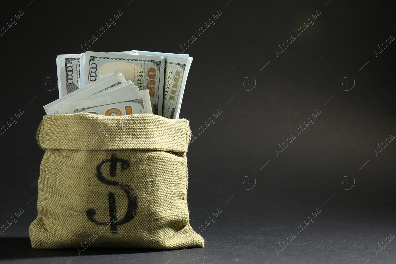 Photo of Dollar banknotes in burlap sack on dark background, space for text