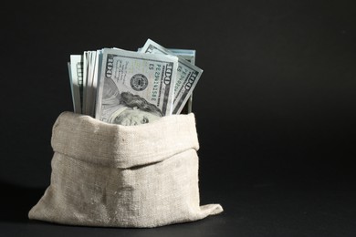 Photo of Dollar banknotes in burlap sack on dark background, space for text